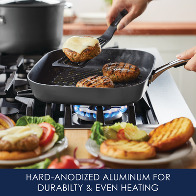 Grilled patties on a frying pan over a gas stove, with plated food nearby.