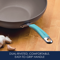Frying pan with a teal handle on a wooden surface, garlic beside it.