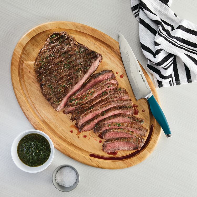 Sliced steak on a wooden board with knife and seasoning bowls nearby.