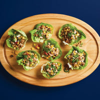 Lettuce wraps with corn and herbs on a wooden platter.