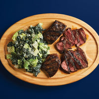 Grilled steak slices with a Caesar salad on a wooden platter.