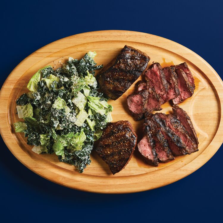 Grilled steak slices with a Caesar salad on a wooden platter.