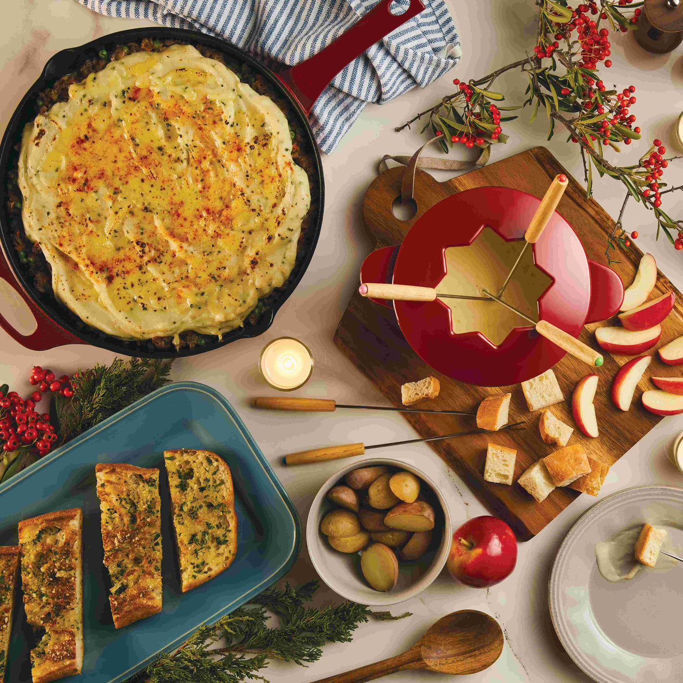 A table with fondue, shepherd's pie, bread, apples, and festive decor.