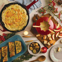 A table with fondue, shepherd's pie, bread, apples, and festive decor.