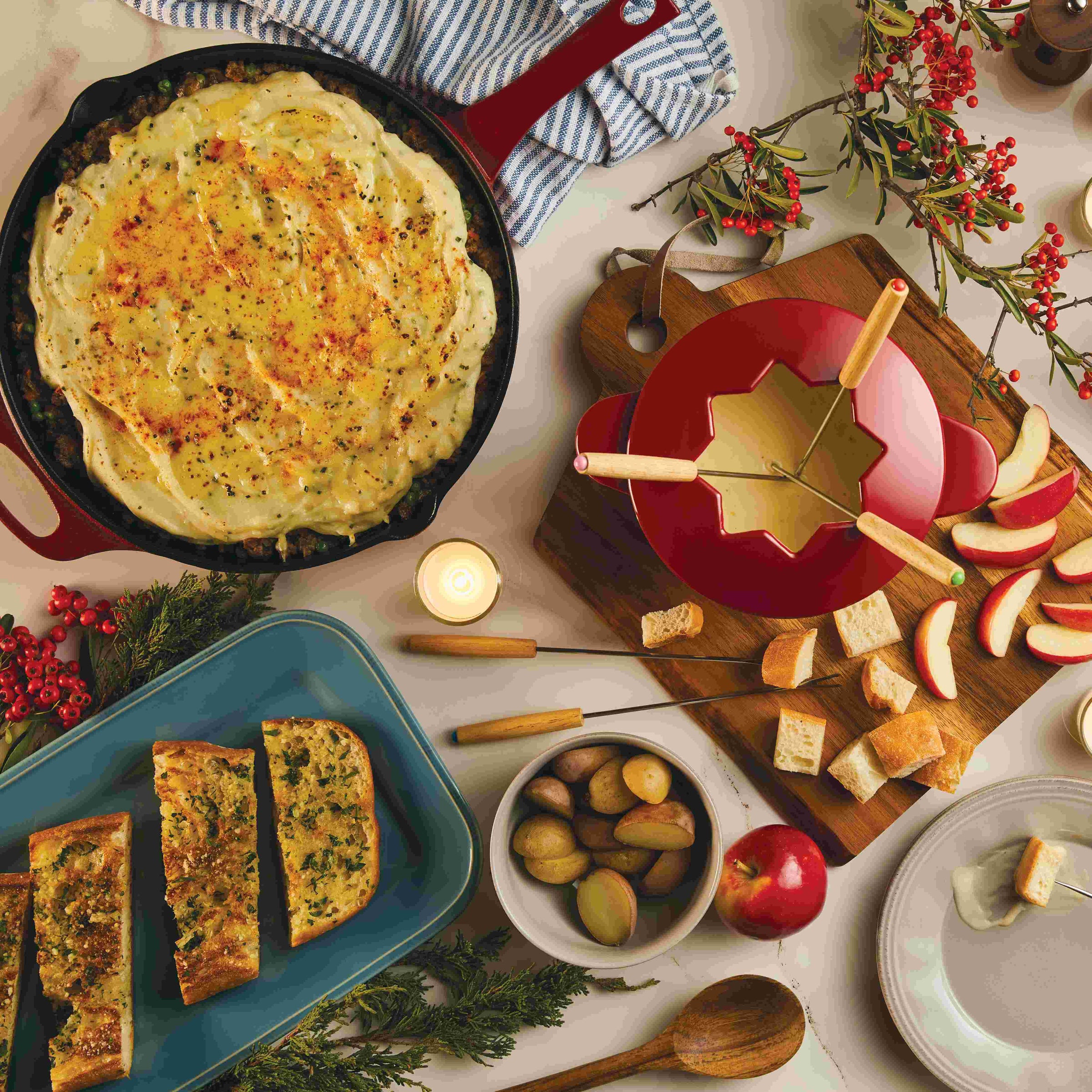A table with fondue, shepherd's pie, bread, apples, and festive decor.