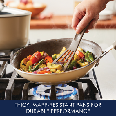 Stirring vegetables in a pan on a stove with a slotted spatula.