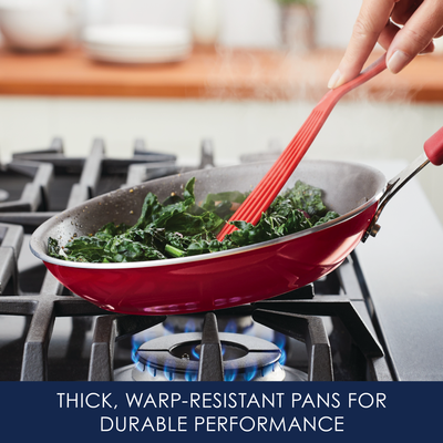 Red frying pan with greens on a lit gas stove, red spatula stirring.