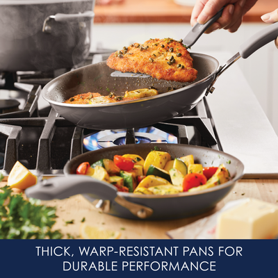 Frying pans on a stove with fish and vegetables cooking.