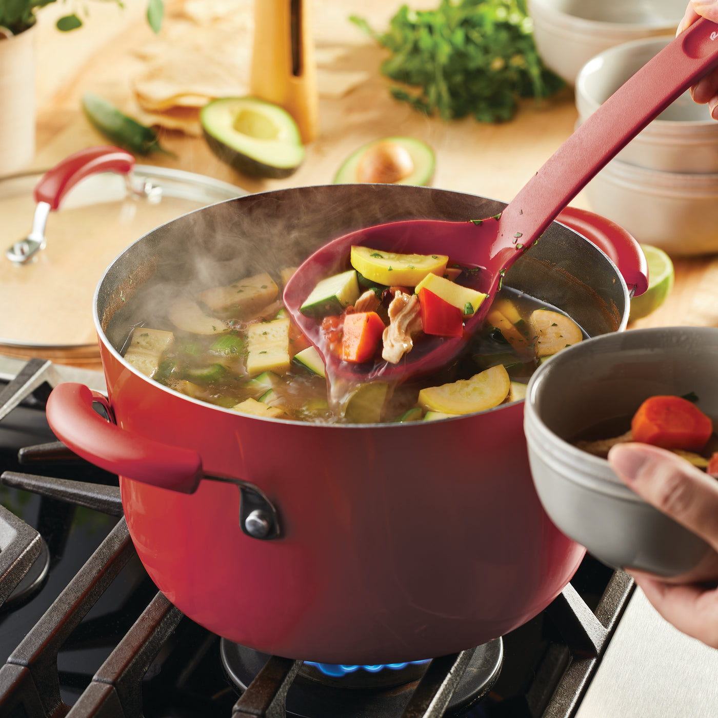 Ladle of vegetable soup served from a red pot on a stove.