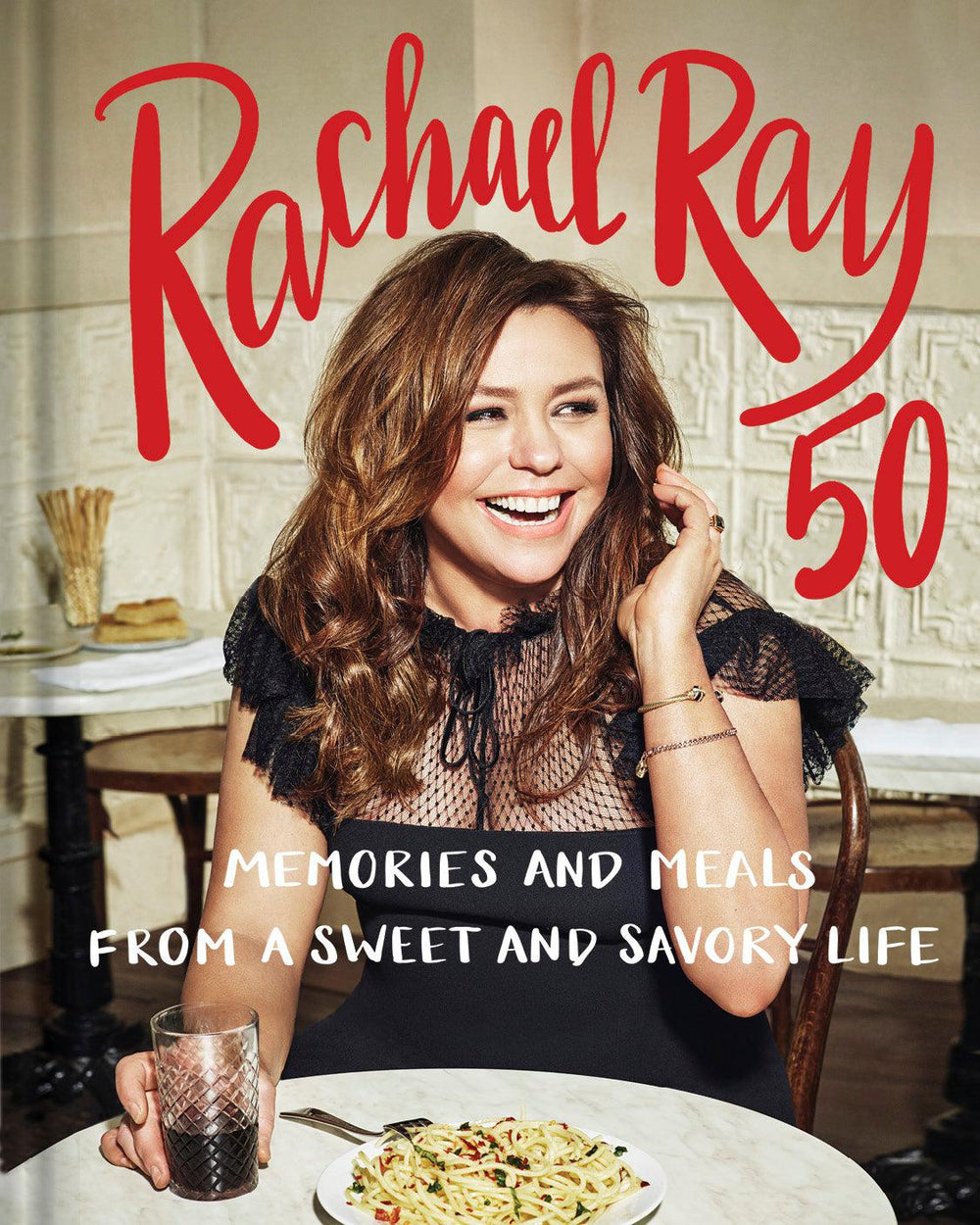 Woman smiling at table with pasta, drink, and book title "Rachael Ray 50".