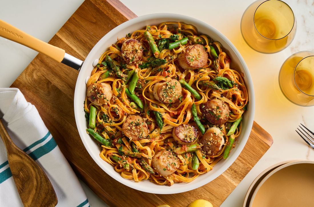 Seared scallops with lemon-scented breadcrumbs and asparagus served over saffron fettuccine in a cream-colored Rachael Ray Cucina skillet.