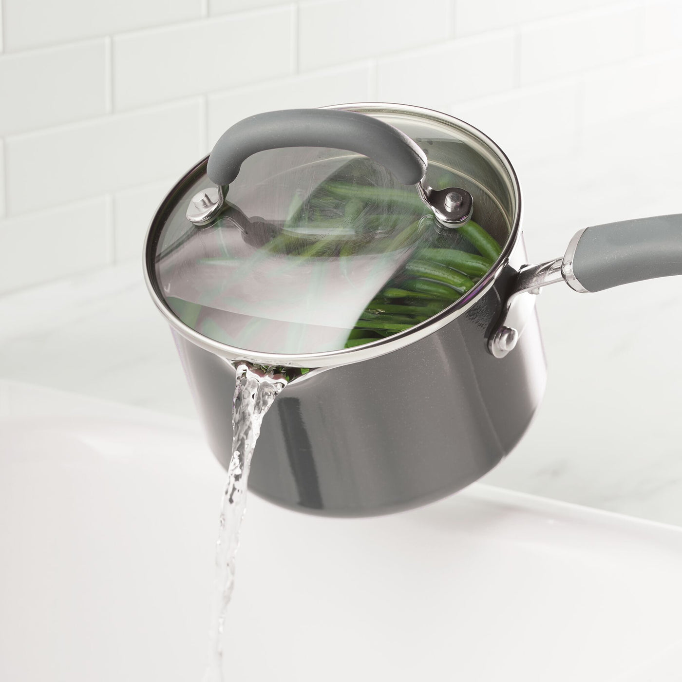 Pot with strainer lid draining water from green beans in a kitchen.