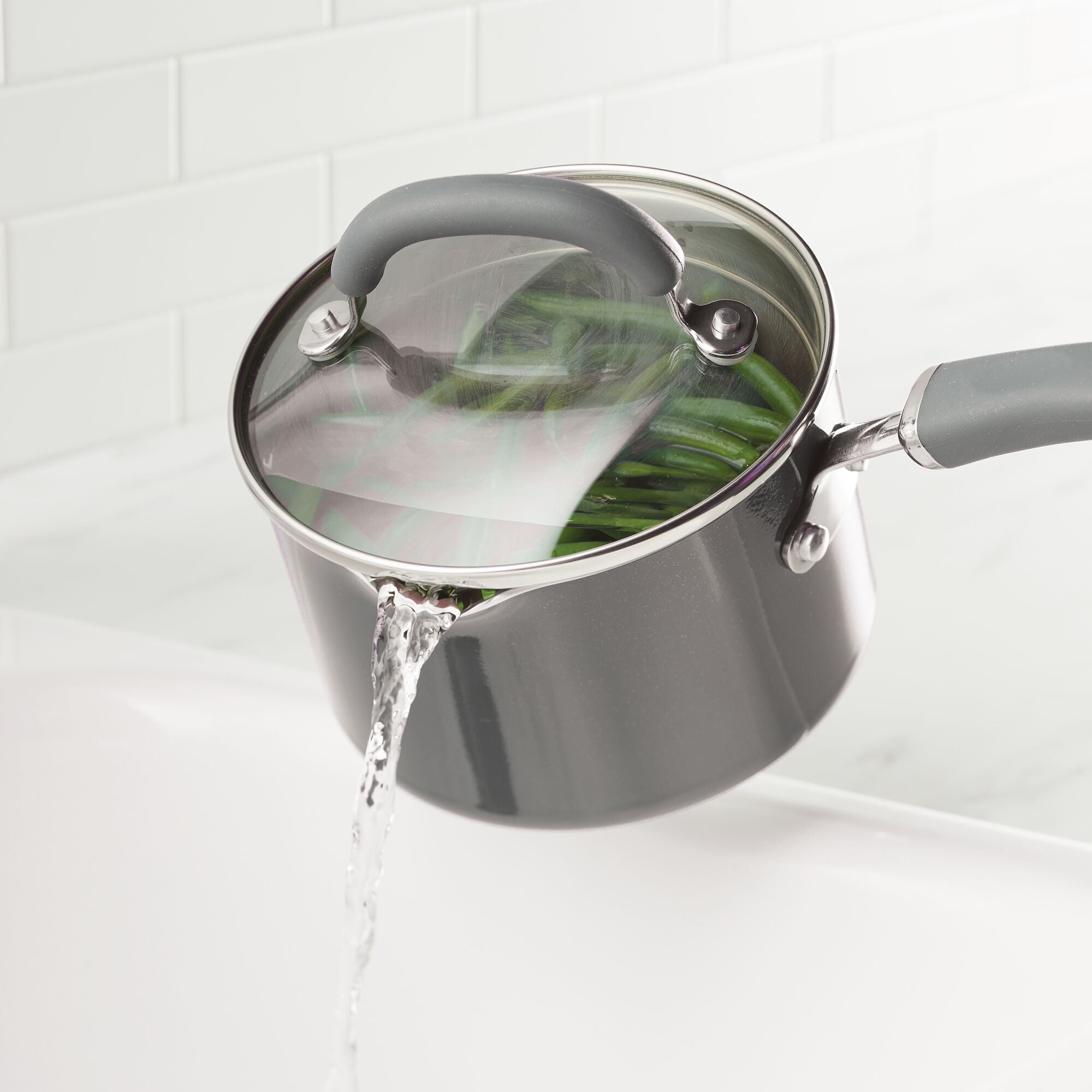 Pot with strainer lid draining water from green beans in a kitchen.