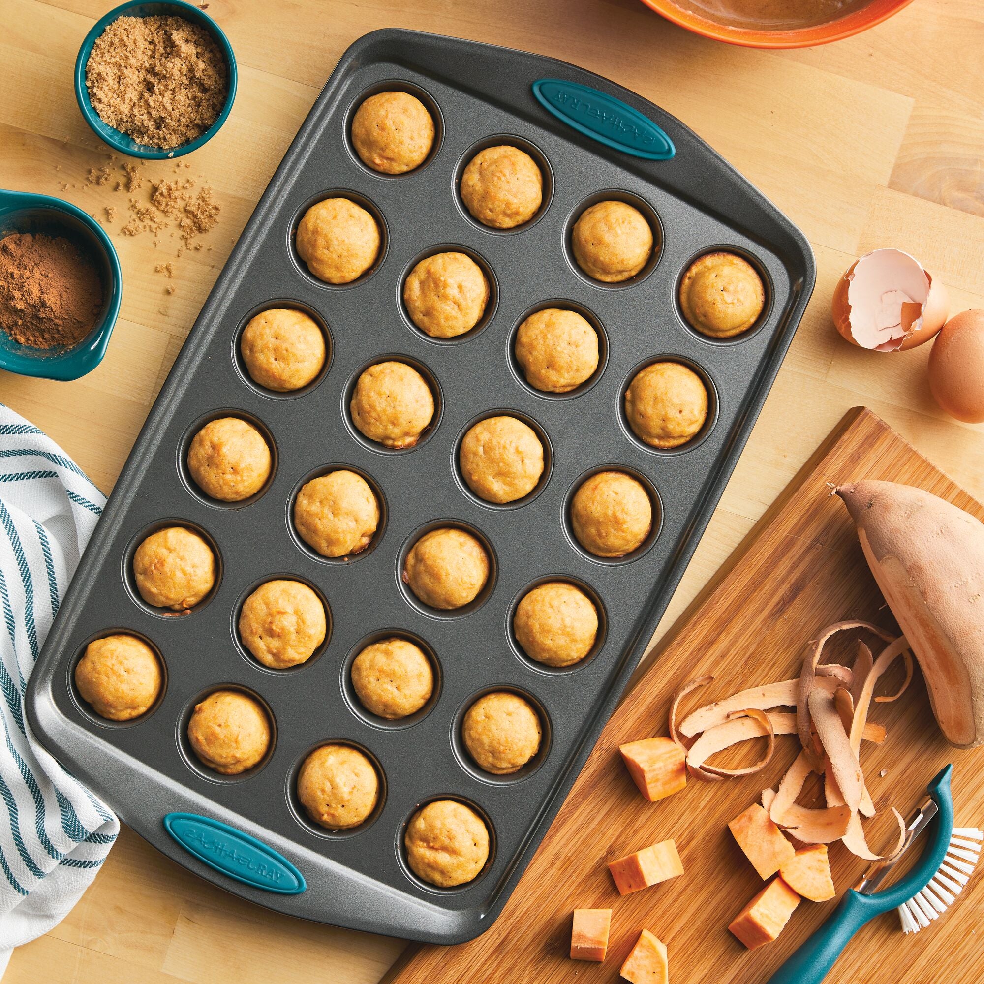 Muffin pan with baked mini muffins, surrounded by ingredients and utensils.