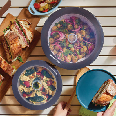 Food storage lids covering dishes and sandwiches on a wooden table.