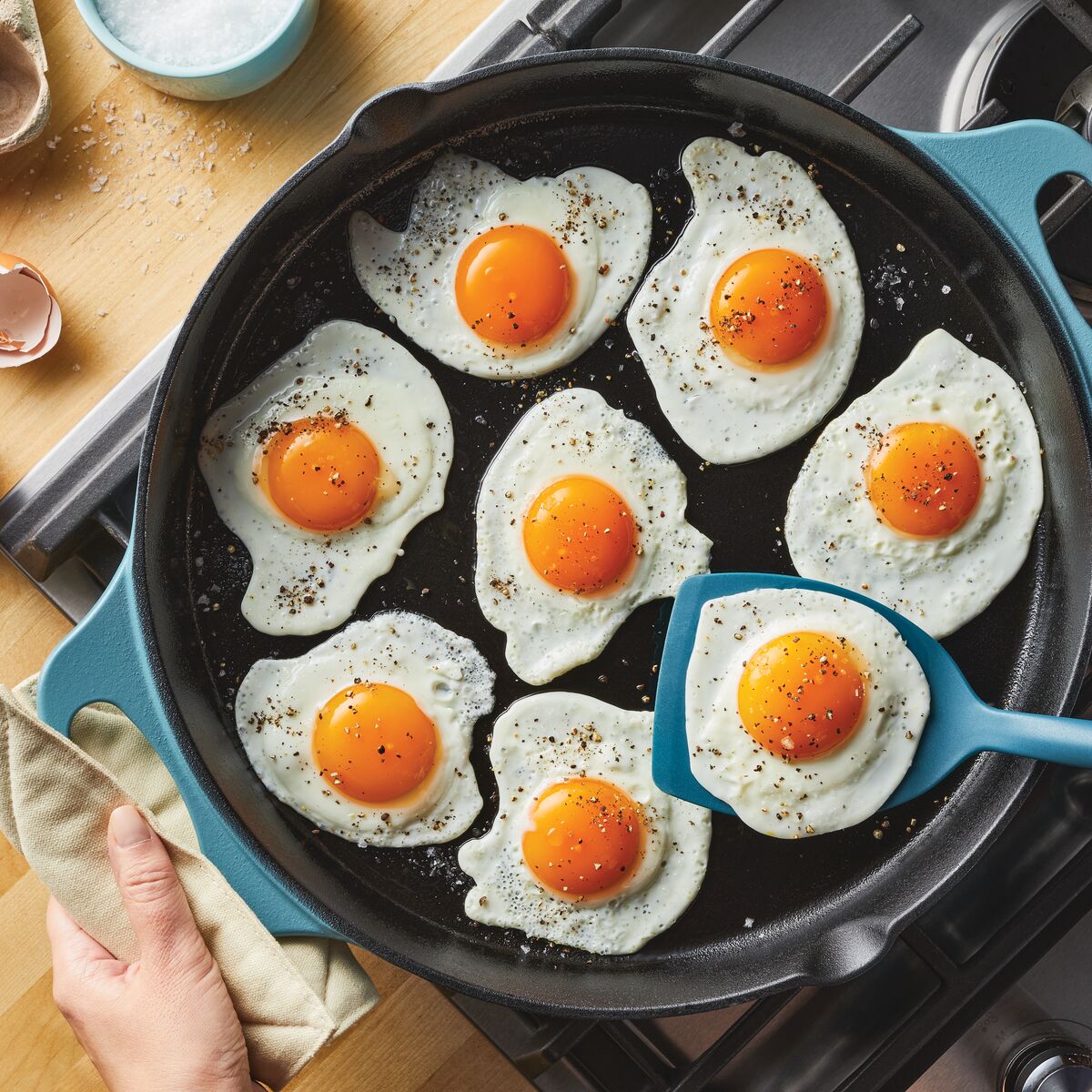 Seven sunny-side-up eggs sizzle in a 14-Inch NITRO Cast Iron Skillet on the stove, perfectly cooked and ready to enjoy.