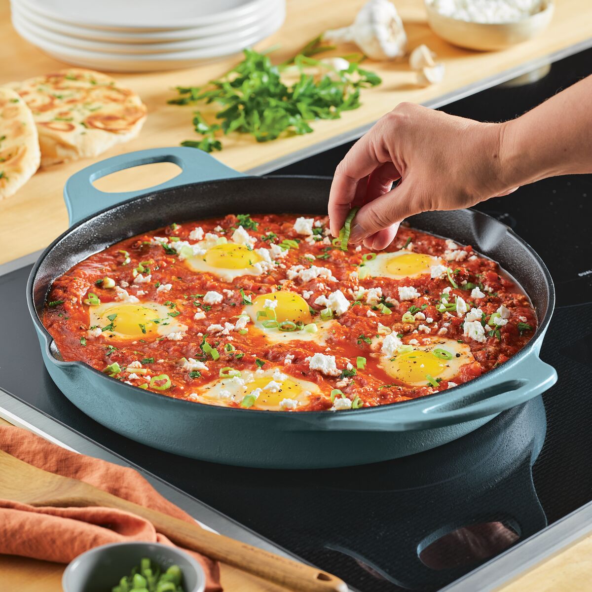 With the 14-Inch NITRO Cast Iron Skillet, someone is expertly seasoning eggs in tomato sauce on a stove. This induction-ready skillet ensures even cooking, and its oven-safe design allows for a seamless transition from stovetop to oven for perfect results.