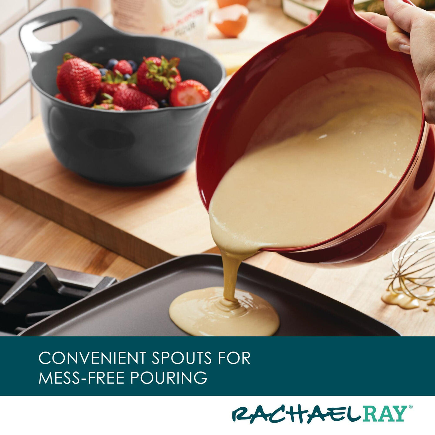 Batter being poured from a red bowl into a pan; strawberries in background.