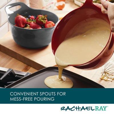 Batter being poured from a red bowl into a pan; strawberries in background.