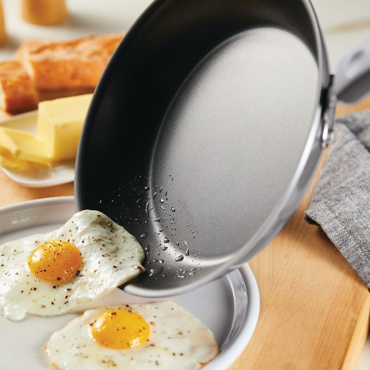 Nonstick pan sliding fried eggs onto a plate near butter and bread.