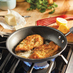 Two breaded chicken fillets frying in a skillet on a gas stove.