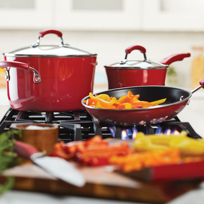 Red cookware on stove with chopped vegetables being sautéed.