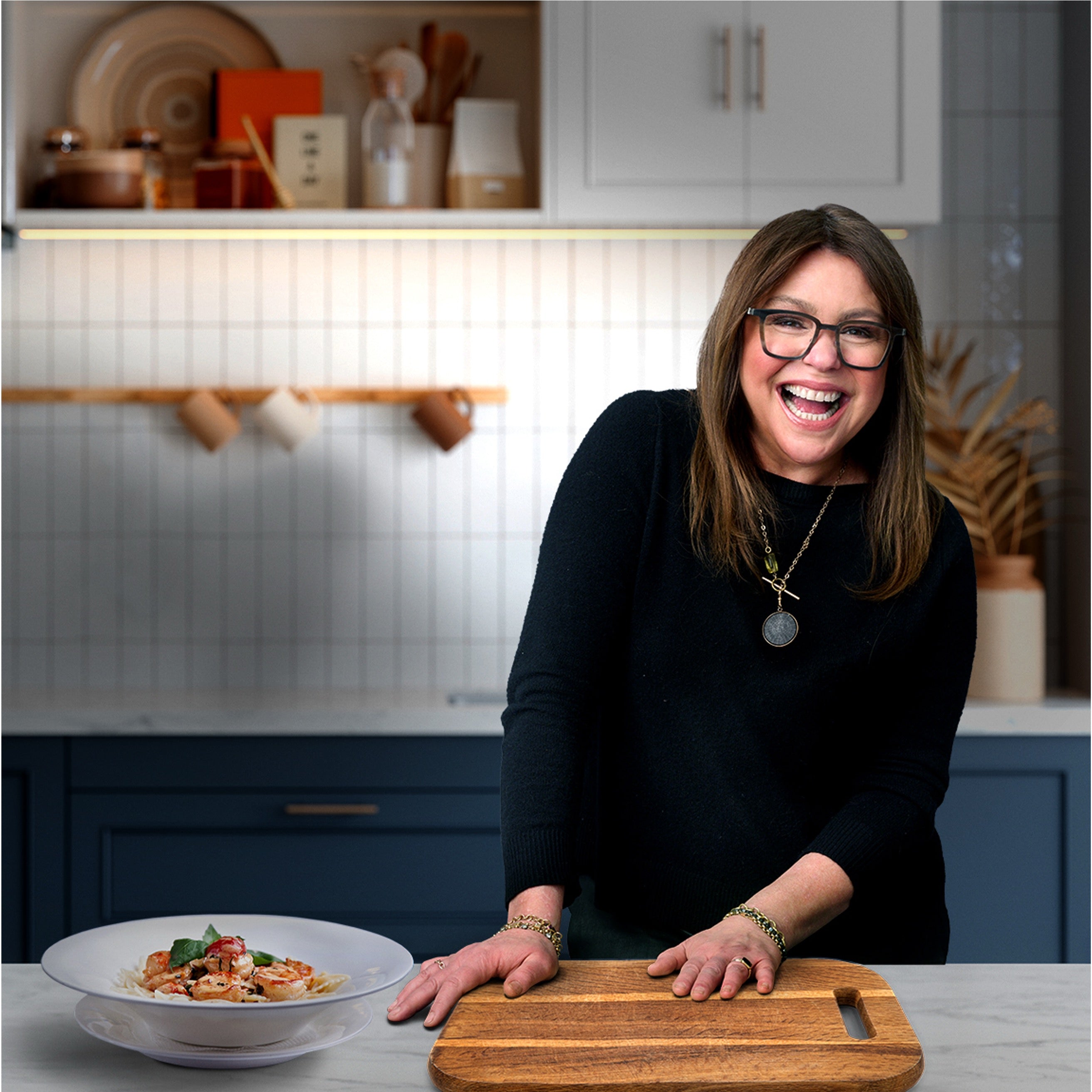 Smiling woman in kitchen with a dish and cutting board.