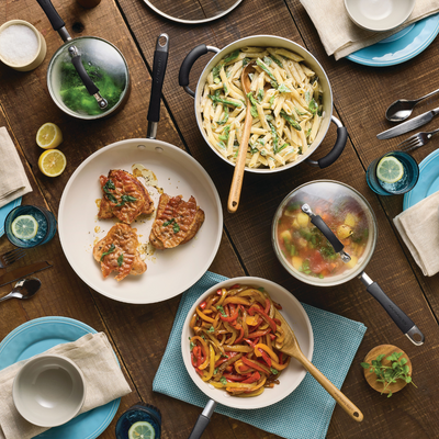 Table set with pasta, cooked pork, sautéed peppers, salad, and utensils.