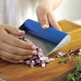 Person using a blue-handled bench scraper to collect chopped onions.