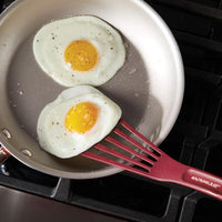Two fried eggs in a pan with a red spatula.