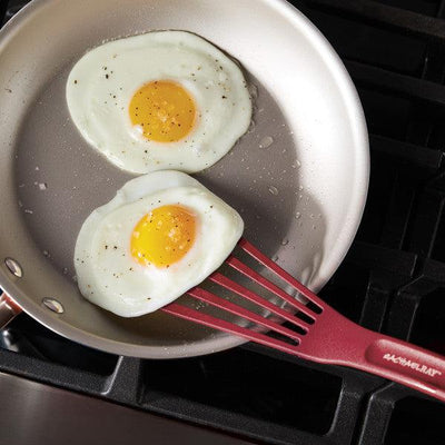 Two fried eggs in a pan with a red spatula.