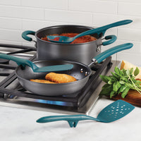 Cooking pots and utensils on a stove with herbs and Parmesan nearby.