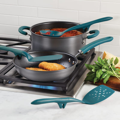 Cooking pots and utensils on a stove with herbs and Parmesan nearby.