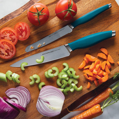 Two knives on a cutting board with sliced vegetables and tomatoes.