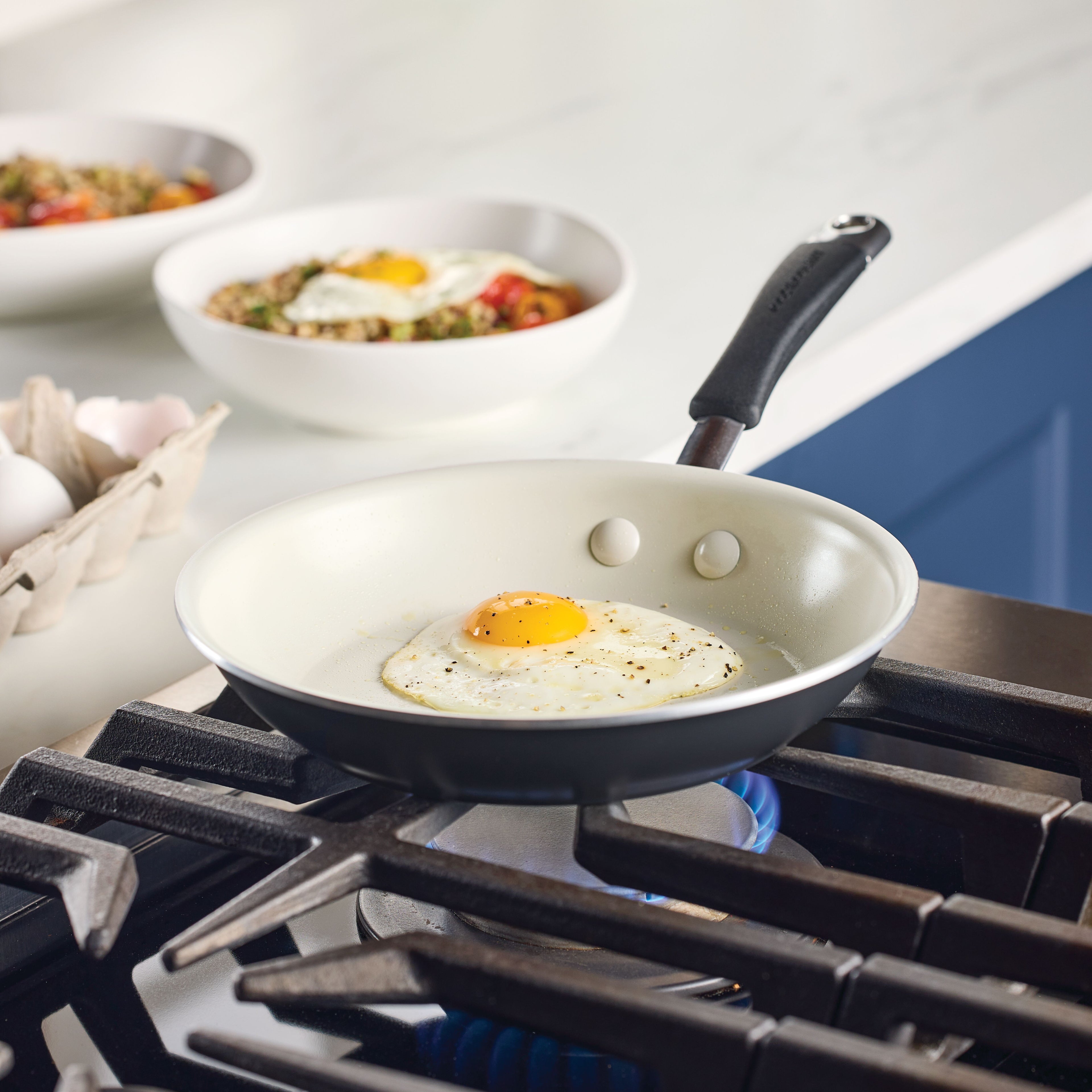 An egg frying in a skillet on a gas stovetop, with bowls of prepared food in the background.