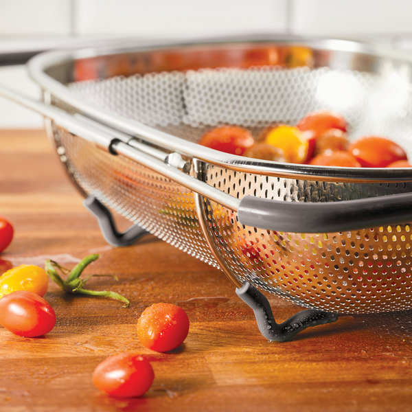 Cherry tomatoes in a metal colander on a wooden surface.