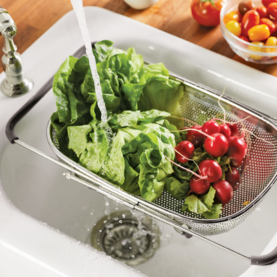 Washing lettuce and radishes in a colander under a kitchen faucet.