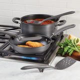 Two non-stick pans on a stove with cooking utensils and basil leaves nearby.