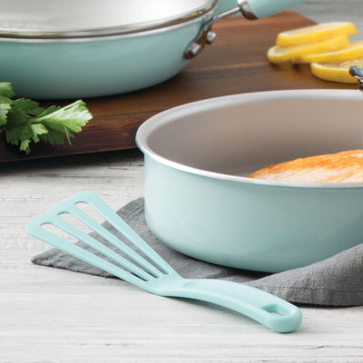 Light blue frying pan and spatula on a counter with sliced lemons.