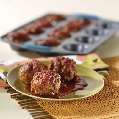 Three meatloaf muffins with sauce on a plate, muffin tray in background.