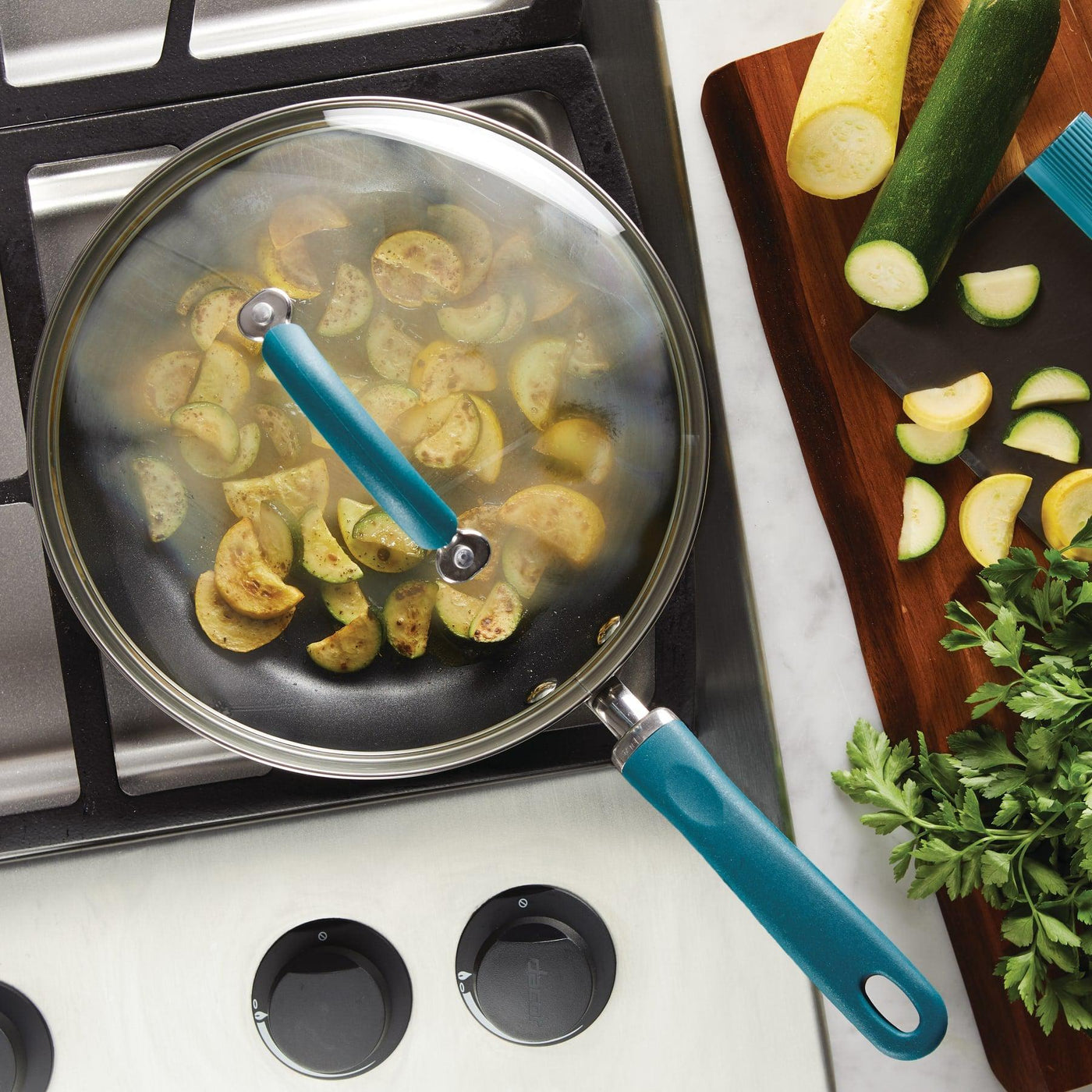 Sliced zucchini cooking in a covered pan on a stovetop, with fresh ingredients.