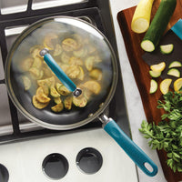 Sliced zucchini cooking in a covered pan on a stovetop, with fresh ingredients.