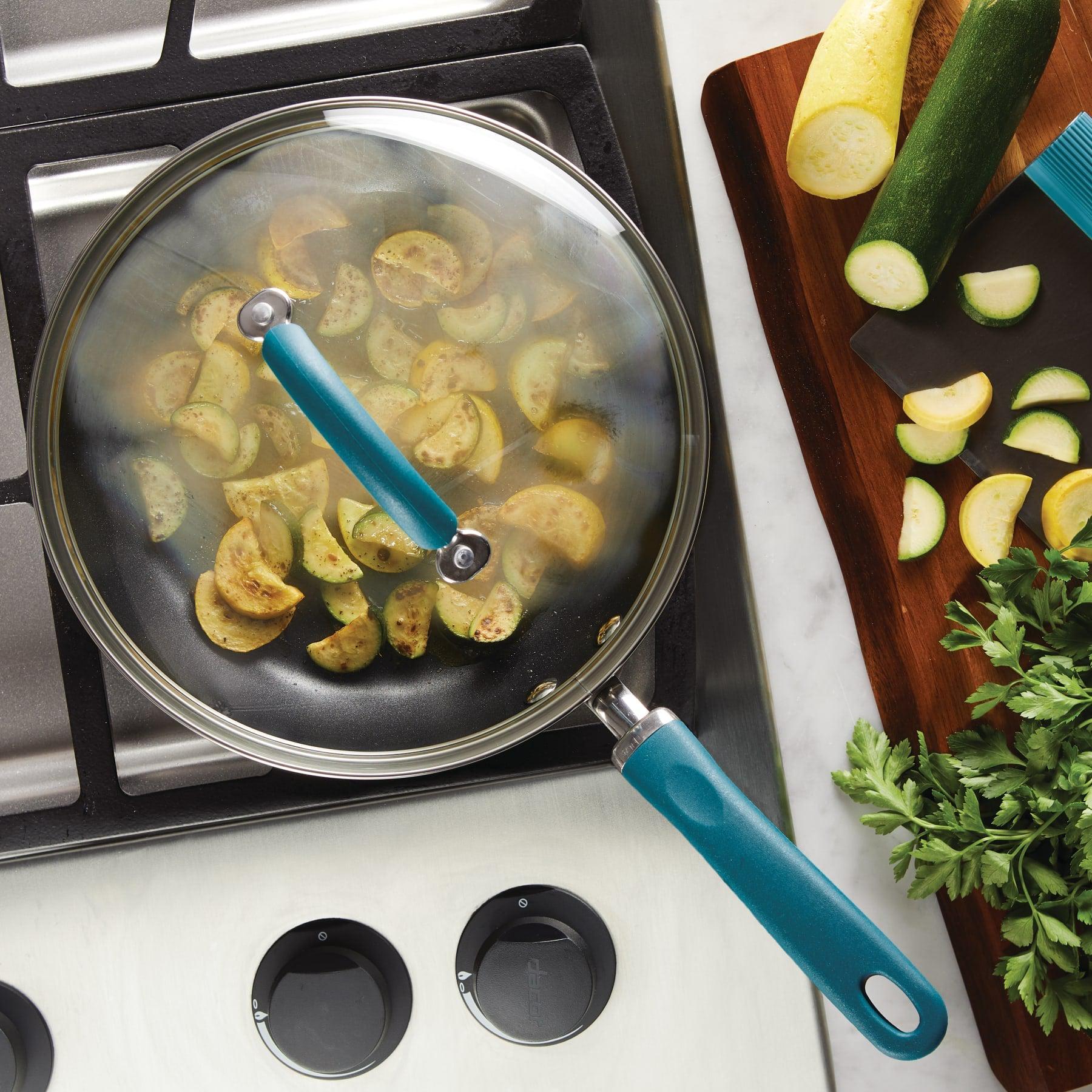 Sliced zucchini cooking in a covered pan on a stovetop, with fresh ingredients.