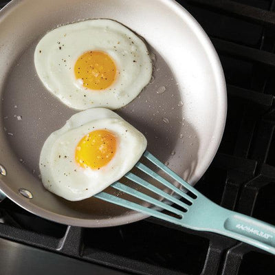 Two sunny-side-up eggs in a frying pan, one being lifted by a spatula.