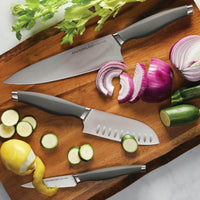 Three knives on a cutting board with zucchini, onion, and a peeled lemon.