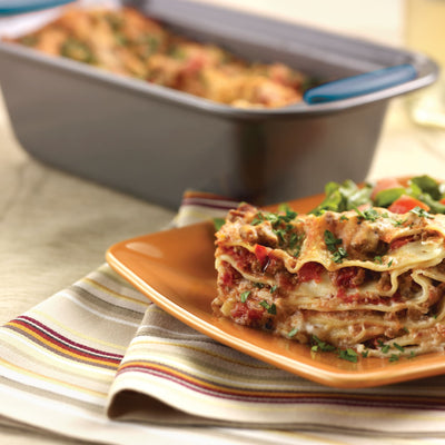 Slice of lasagna on a plate, with a baking dish in the background.