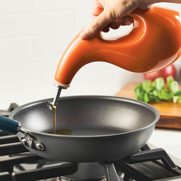 Pouring oil with precision from a 24-ounce EVOO Bottle featuring a stainless steel pour spout into a frying pan on the stove.