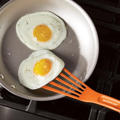 Two sunny-side-up eggs in a frying pan with an orange spatula.