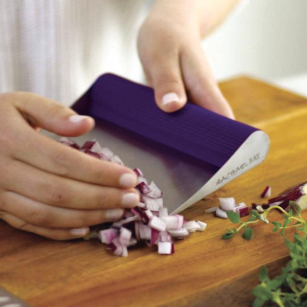 Using the Bench Scrape - Rachael's Food Mover with a purple handle on a wooden board to chop onions.