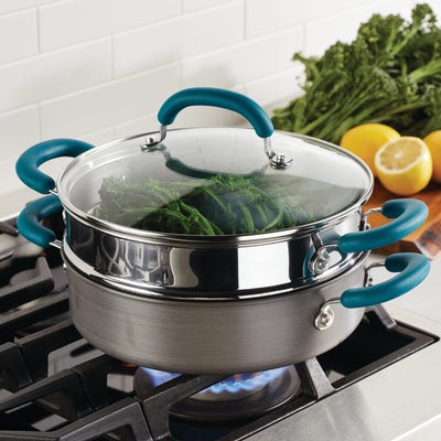 Steamer pot on stove cooking greens with a glass lid and blue handles.